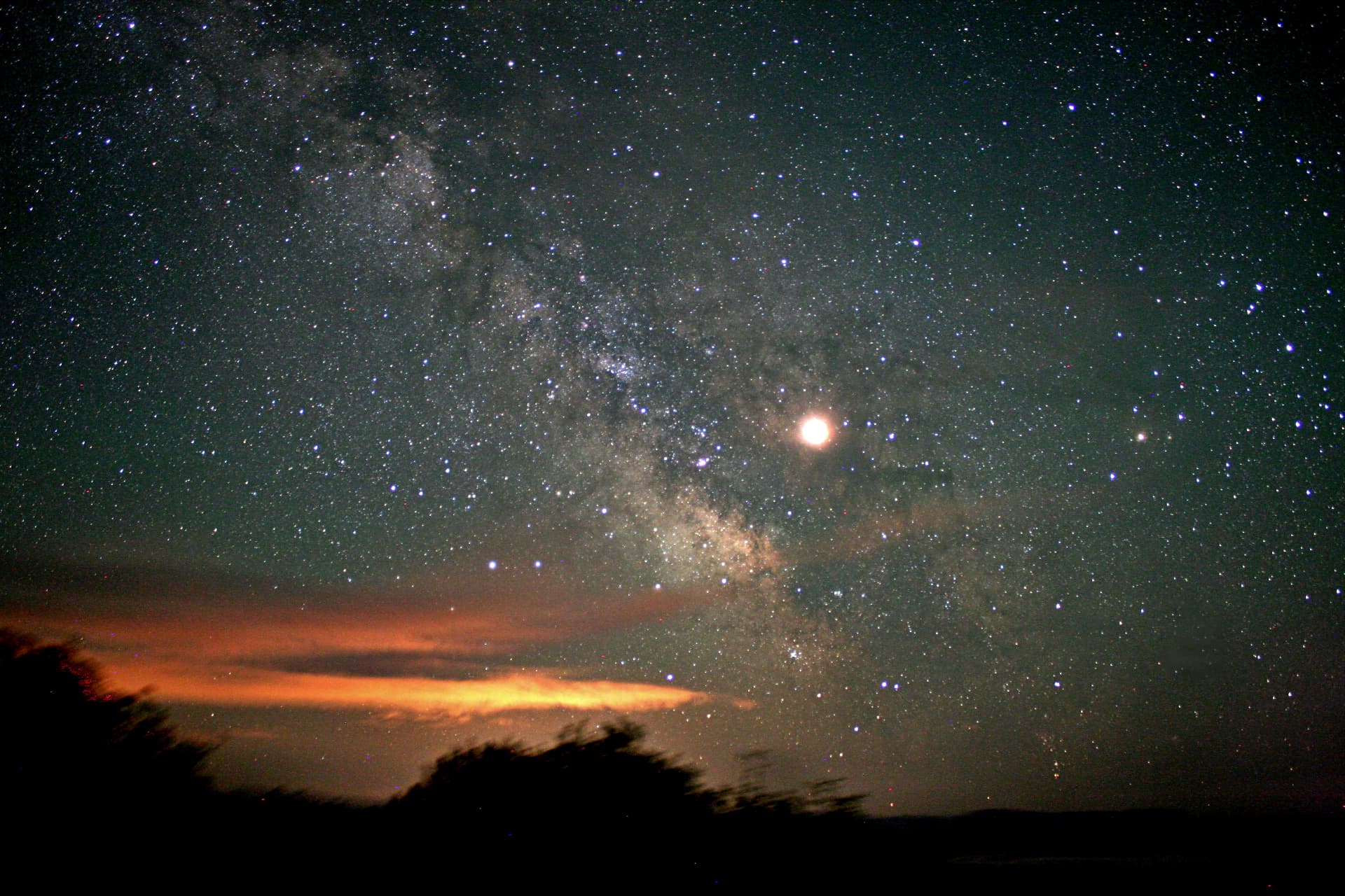 The Milky Way rising past a bright Moon above a dark horizon